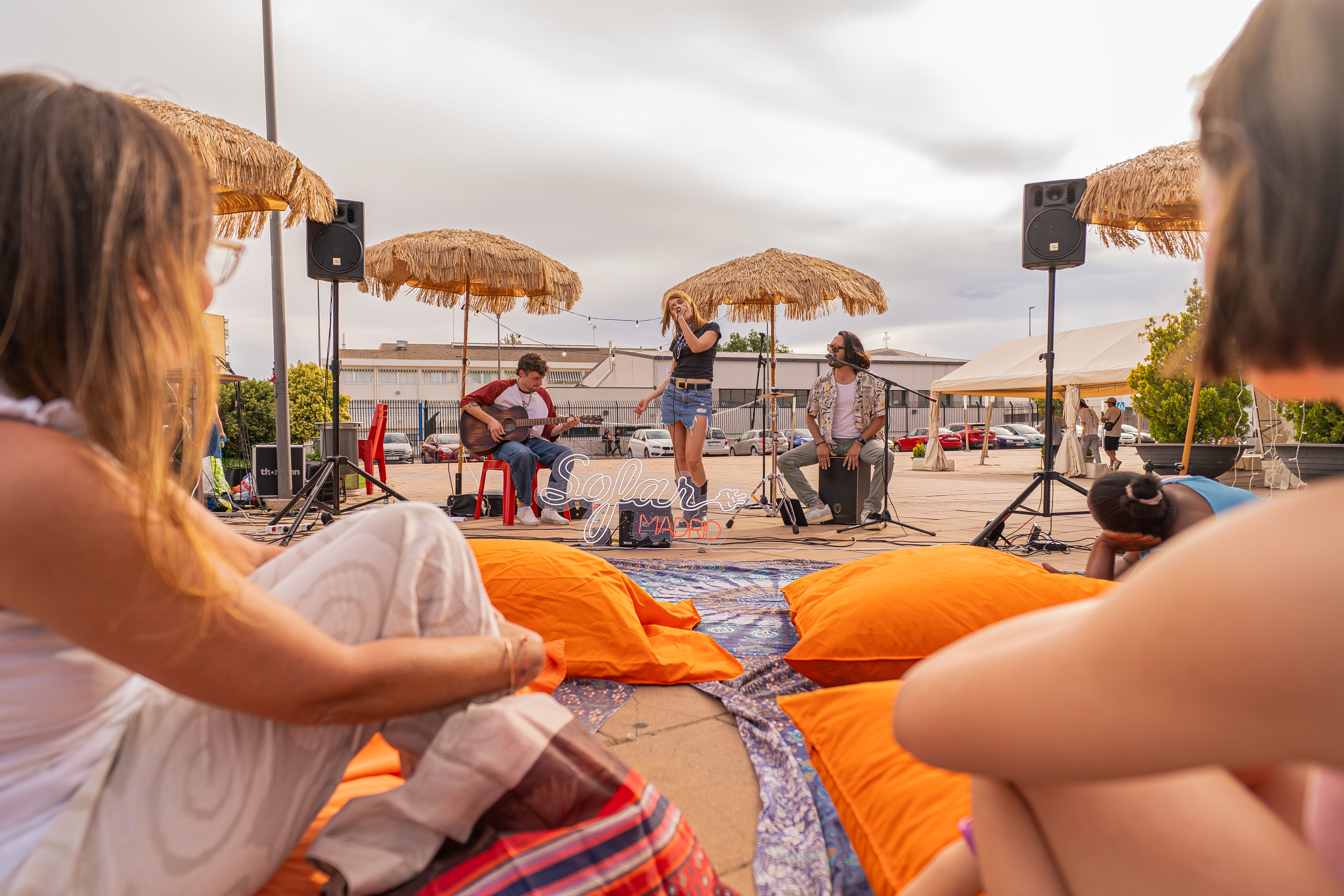 Outdoor live music festival with an audience gathered beneath straw umbrellas.